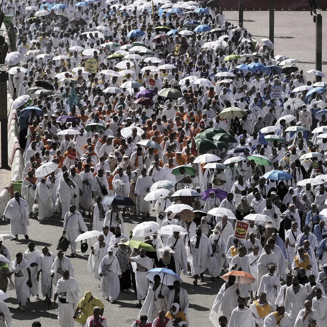Hajj pilgrims walking with umbrellas in warm weather